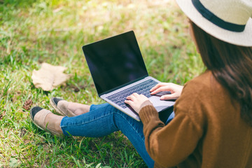 Closeup image of a woman working and typing on laptop keyboard while sitting in the outdoors