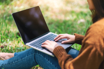 Fototapeta premium Closeup image of a woman working and typing on laptop keyboard while sitting in the outdoors