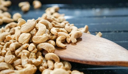 Group of Cashew nuts on wooden ladle in black baking tray