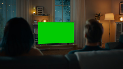 Couple Watches Green Mock-up Screen TV while Sitting on a Couch in the Living Room. Romantic...