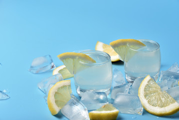 Glasses of limoncello on a blue background among ice and lemon slices