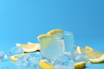 Glasses of limoncello on a blue background among ice and lemon slices