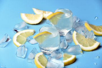 Glasses of limoncello on a blue background among ice and lemon slices