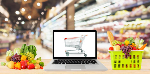 supermarket aisle blurred background with laptop computer and shopping cart on wood table grocery online concept