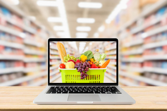 supermarket aisle blurred background with laptop computer and shopping basket on wood table grocery online concept