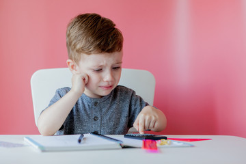 Portrait of cute kid boy at home making homework. Little concentrated child writing with colorful pencil, indoors. Elementary school and education. Kid learning writing letters and numbers