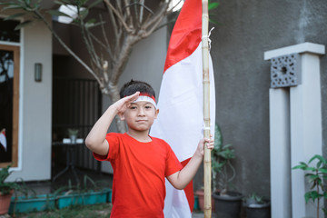 portrait of asian kid saluting while holding indonesia flag