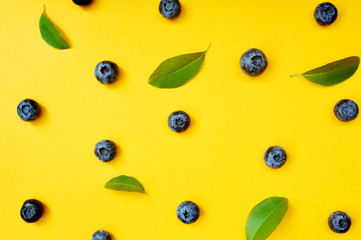 Fototapeta premium Summer blueberries with leaf on yellow background. Berries design backdrop. Close up top view or flat lay