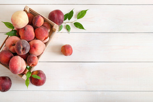 Ripe peaches in a box on wooden background top view