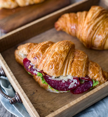 Croissant sandwich on the wooden table with salami, cheese and fresh salad food photography