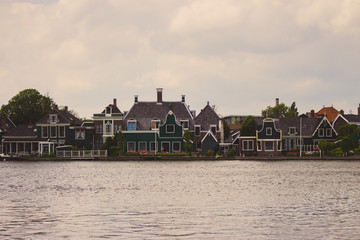 Obraz premium Typical dutch buildings on the river side faded. Holland architecture filtered. Country houses in Zaanse Schans, Netherlands. Rural buildings on the lake. Summer travel concept. Summer countryside.