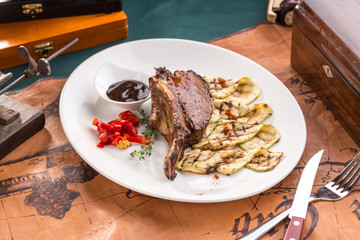 Pork Brisket with grilled zucchini and chili pepper on white plate on old map background