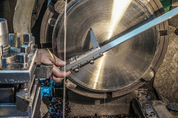The worker on the lathe makes measurement with a caliper of the manufactured part.