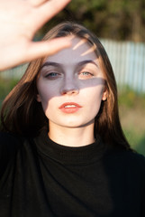A young girl covers her face with her hand. The sun's rays fall on the face and hands of a girl in...