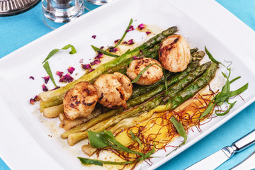  European recipe, Mediterranean dish. Caramelized asparagus with onion chips, rose petals, arugula and pieces of fried fish