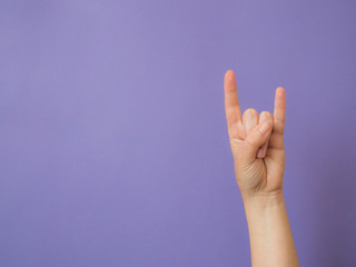 Female hand shows sign "devil" on purple background with copy space