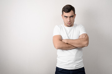 Portrait of a serious, angry young man with folded arms in a white t-shirt with a copy of space
