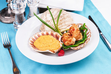 European recipe, Mediterranean dish. Baked mollusk in the oven under a cheese cap, served with crispy fish slices and greens, onions and red pepper according to a national recipe
