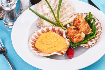 European recipe, Mediterranean dish. Baked mollusk in the oven under a cheese cap, served with crispy fish slices and greens, onions and red pepper according to a national recipe
