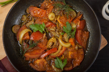 fried tomatoes with onions and parsley in a pan close-up. View from above.