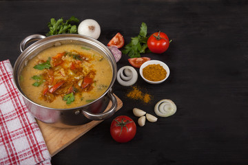 Asian red lentil soup in a pan on a black wooden background. Onions, garlic, tomatoes and spices.