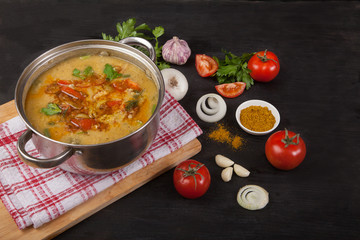 A red lentil soup casserole stands on a napkin on a black background. Near onion, garlic and spices.