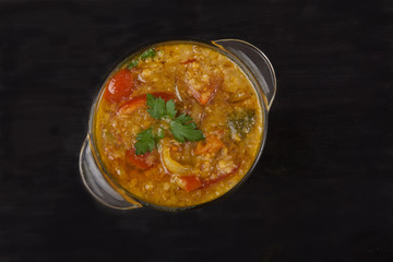 Red lentil soup in a glass bowl with spices, herbs, onion and garlic on a black background. Copy spaes.