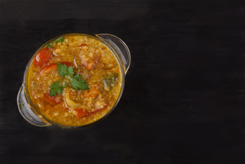 Red lentil soup in a glass bowl with spices, herbs, onion and garlic on a black background. Flat lay.