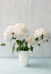 Garden white peonies with lilac border in a white porcelain vase  on a light blue wooden background, close up