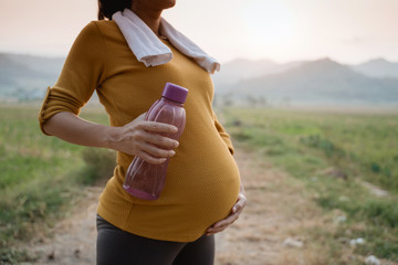 close up of pregnant belly with bottle of water while exercising