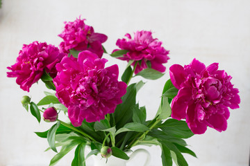 Purple garden peonies in a white enamel jug on a white wooden background, rustic style, close up