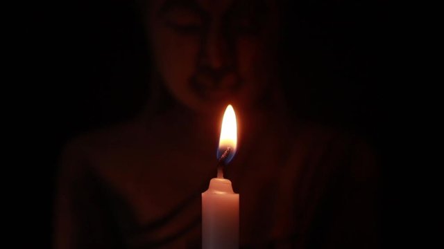 Lighting white candle and blowing it out with face buddha statue on black background