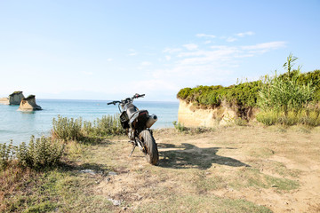 A motorcycle on the sandy cliff on the blue sky and ocean view in distance.