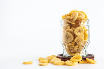 Dried banana slices in glass bottle with wooden saucer isolated on white background