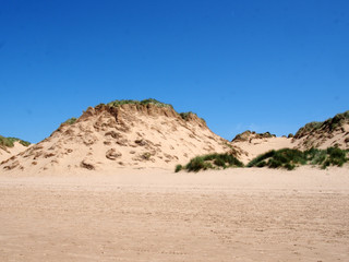 the beach at formby merseyside with tall sand dunes covered in rough grass and a blue summer sunlit sky