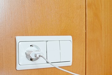 Close up of an power supply equipment and an charger plugged in on wooden wall.