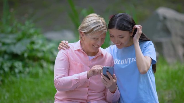 Mature woman and young volunteer looking smartphone photos together, assistance