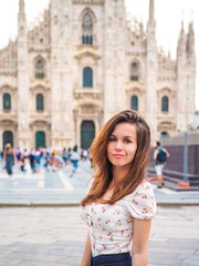 Brunette girl with long hair in a gentle way walks in the square of Milan and poses on the background of the Milan Cathedral