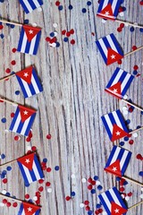 Fototapeta premium October 10, happy independence Day of Cuba. the concept of patriotism , freedom and independence. Mini flags with paper confetti on wooden background, vertical