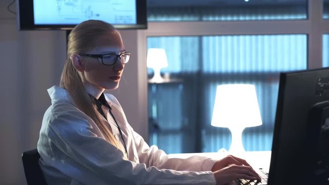 Female electronics engineer working on the computer and writing the results of the research in laboratory. Woman is in white coat and glasses
