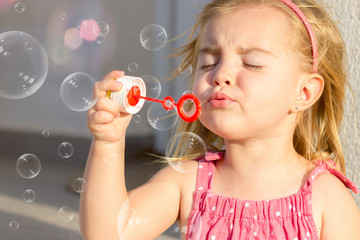 A cute blonde little girl playing with soap bubbles