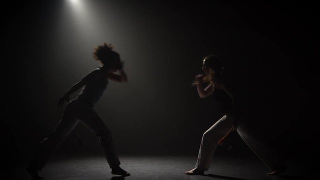 Capoeira in darkness under spotlight at studio on black background