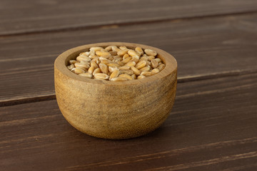 Lot of whole fresh beige dinkel wheat grain in a wooden bowl on brown wood