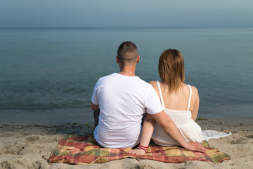  Young pregnant couple relaxing on beach, sitting together on sand.