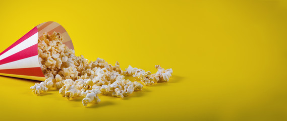 striped cone bag with spilled popcorn on yellow background with copy space