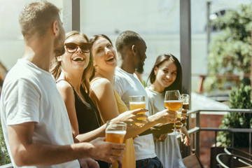 Young group of friends drinking beer, having fun, laughting and celebrating together. Women and men with beer's glasses in sunny day. Oktoberfest, friendship, togetherness, happiness, summer concept.