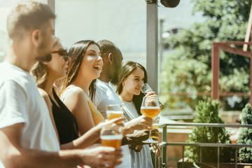 Young group of friends drinking beer, having fun, laughting and celebrating together. Women and men with beer's glasses in sunny day. Oktoberfest, friendship, togetherness, happiness, summer concept.