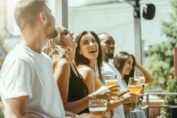 Young group of friends drinking beer, having fun, laughting and celebrating together. Women and men with beer's glasses in sunny day. Oktoberfest, friendship, togetherness, happiness, summer concept.