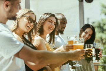 Young group of friends drinking beer, having fun, laughting and celebrating together. Women and men with beer's glasses in sunny day. Oktoberfest, friendship, togetherness, happiness, summer concept.