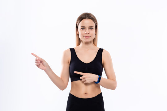Young sporty blond woman in a black sportswear with smart watches for pulse measuring pointing with fingers to the left.